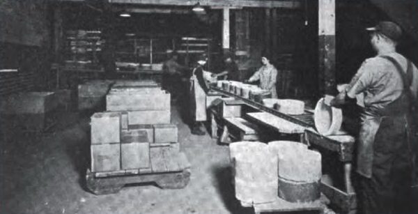 The three operations in this porcelain plant were conveyors have demonstrated their value -- (1) loading the kilns, (2) unloading the kilns, and (3) inspecting and packing.  The conveyor belt shown along the wall serves two purposes.  The upper belt carries the green ware to the portable belt section which takes it into the kilns, as shown in the illustration above.  By means of a special device the saggers of green ware are transferred to the cross belt without damage from jarring.  The lower or return section of the belt carries the fired ware back.  How it is taken out of the kiln on a portable section of roller gravity conveyor is shown in the second illustration and explained in the item.  The porcelain is placed in saggers, the large white, circular containers seen on the belt conveyor.  These protect the green ware when handling and while firing.  The inspecting and packing are done on the conveyor at the right.